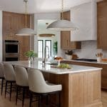 Modern kitchen with light wood cabinets, white marble island, and pendant lights.