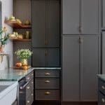 Dark gray kitchen cabinets with brass hardware and green marble countertops.