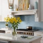 White kitchen with blue subway tile backsplash, marble island, and yellow lilies