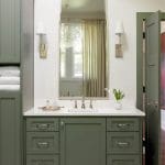 Green bathroom vanity with white countertop, silver hardware, and sconce lighting.