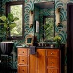 Bathroom with green art deco wallpaper, wood vanity, and black hex tile floor.