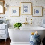 Freestanding white bathtub with brass fixtures, blue and white chinoiserie stool, and floral