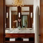 Bathroom with marble vanity, wood cabinetry, brass fixtures, and butterfly chandelier.