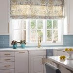 Kitchen with white cabinets, blue subway tile backsplash, and patterned roman shade.