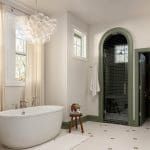 White freestanding bathtub, glass shower with black tile, and bubble chandelier