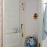 Shower with white subway tile, gold fixtures, and blue and white garden stool.