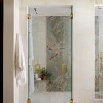 Bathroom with glass shower enclosure featuring a marble accent wall and gold hardware.