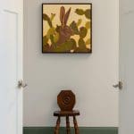 Painting of rabbit and cacti above wooden stool with green wainscoting