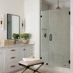 White bathroom vanity with brass hardware, glass shower, and patterned rug.