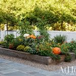 Raised garden bed with pumpkins, mums, and flowers, next to a white brick wall.