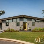 Mid-century modern home with gray brick, a yellow door, and a carport.