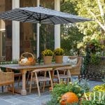 Outdoor dining set with striped umbrella, pumpkins, and fall flowers.