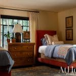 Bedroom with two red-framed beds, blue bedding, floral pillows, and a wooden dresser.