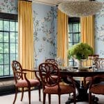 Dining room with floral wallpaper, yellow curtains, and a dark wood table with chairs.