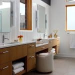 Modern bathroom with wood vanity, white tile, and stone floor. Features dual sinks and a fluffy