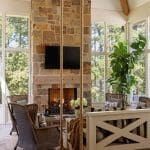 Sunroom with stone fireplace, wicker chairs, and hanging swing.
