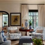 Living room with blue and white floral armchairs, blue patterned ottoman, and round wooden table.