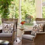 Sunroom with wicker chairs, floral pillows, and a vase of flowers.
