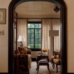 Living room with patterned sofa and chairs, dark wood archway, and window overlooking greenery.