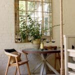 Round metal table with wine glasses and bottle, wooden chair with pillows, gold arched mirror