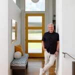 Man leaning against wall in entryway with yellow door and patterned bench