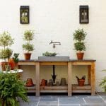 Outdoor sink area with concrete basin, wooden counter, potted plants, and brick wall