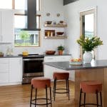 Modern kitchen with white cabinets, stainless steel range, gray island, and rust-colored stools.