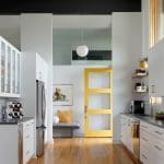 Modern kitchen with white cabinets, stainless steel appliances, and a bright yellow door.