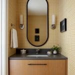 Powder room with yellow grid wallpaper, wood vanity, dark countertop, and oval mirror