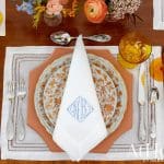 Table setting with blue and orange floral plates, white napkins with monogram, and amber glasses.
