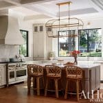 Kitchen with cream cabinetry, marble island, rattan stools, and coffered ceiling.
