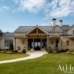 Stone and stucco house with metal roof, covered porch, and manicured lawn.