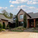Stone house with dark roof, large windows, and wooden porch columns.