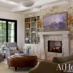 Living room with stone fireplace, built-in bookshelves, and leather ottoman.