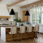 Kitchen with white cabinets, wood island, marble counters, and black pendant lights.