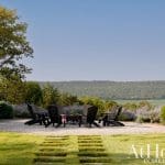 Adirondack chairs around a fire pit with a scenic view of hills and water