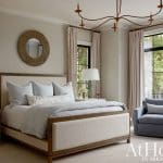 Bedroom with upholstered bed, blue armchair, and large windows overlooking trees.
