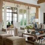 Living room with neutral upholstered chairs, stone fireplace, and large windows