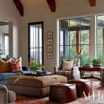 Living room with navy sofa, plaid armchairs, large ottoman, and large windows overlooking trees