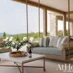 Porch with hanging daybed, striped pillows, coffee table, and outdoor seating.