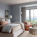 Bedroom with blue walls, tufted headboard, floral bedding, and two orange plaid armchairs.