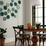 Dining room with decorative plates on wall, round wooden table, and chairs.