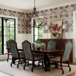 Dining room with patterned wallpaper, dark wood table and chairs, and ornate chandelier.