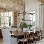 Dining room with stone accent wall, wooden table and chairs, and large vase with greenery.
