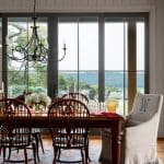 Dining room with wooden table, chairs, chandelier, and view of landscape through glass doors.