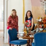 Two women in a dining room with blue velvet chairs and a table set for a meal.