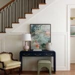 Entryway with navy console table, abstract art, upholstered chair, and staircase