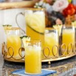 Yellow cocktails with pineapple garnishes on a gold tray with floral arrangement