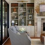Living room with gray striped chairs, built-in bookshelves, and stone fireplace