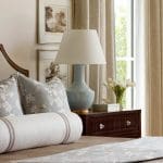 Bedroom with floral pillows, bolster, and a light blue lamp on a nightstand.